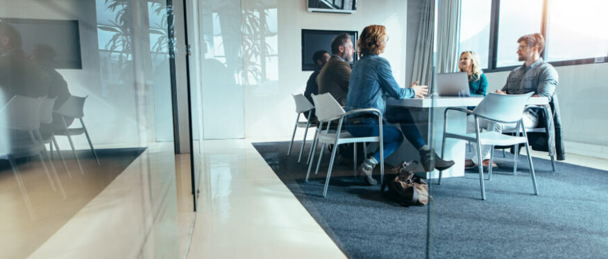 Teammeeting mit vier Personen, das Konzeptzeichnungen im Hintergrund bespricht.