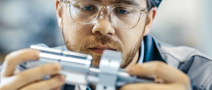 Ingenieur prüft konzentriert ein Metallbauteil im Detail.