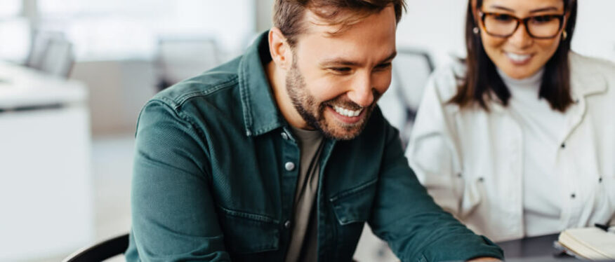Zwei junge Menschen lächeln bei der Arbeit am Laptop.