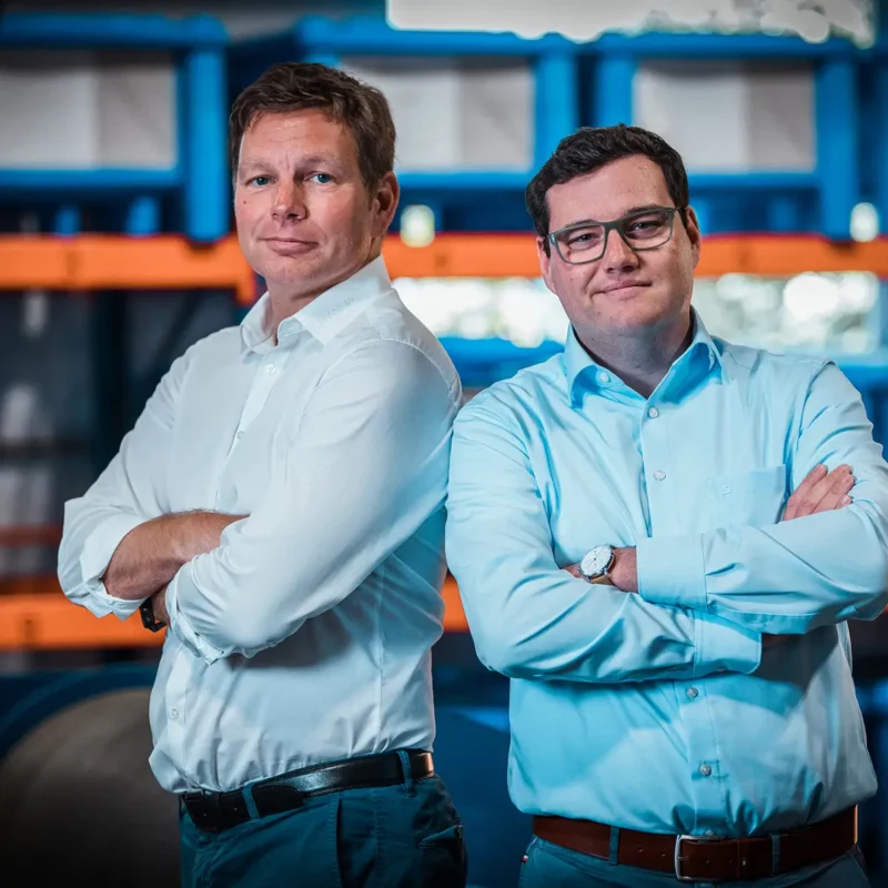 Zwei PLANETA-Geschäftsführer mit verschränkten Armen im Lager – Porträtfoto für Unternehmensdarstellung