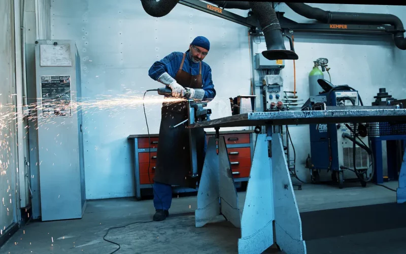 Mitarbeiter mit Schutzkleidung schleift Metallstück – starker Funkenflug in professioneller Werkstattumgebung