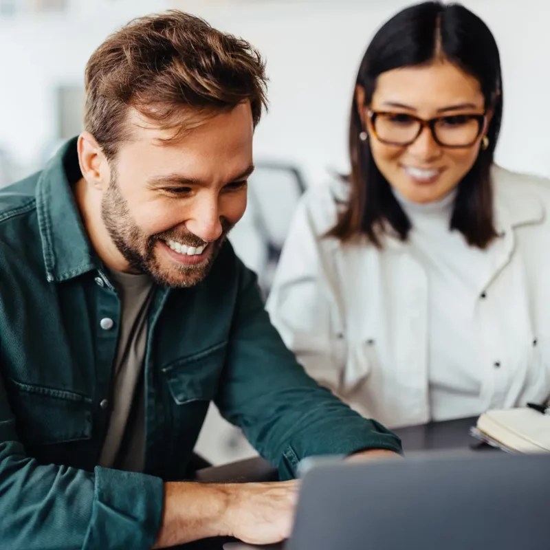 Zwei Mitarbeitende lächeln bei einer digitalen Produktschulung am Laptop